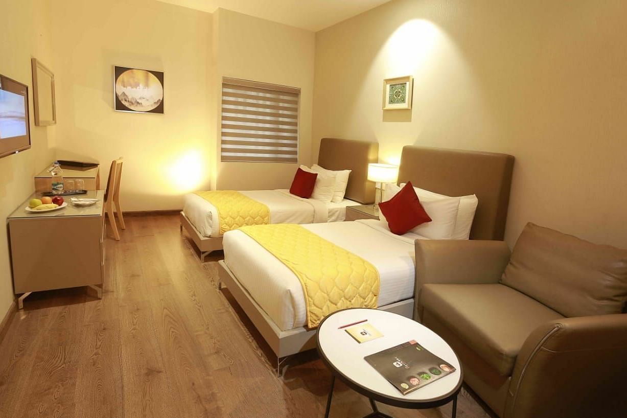Premium Twin Room at Mayberry Tiruppur featuring twin beds, a sofa, and a small coffee table